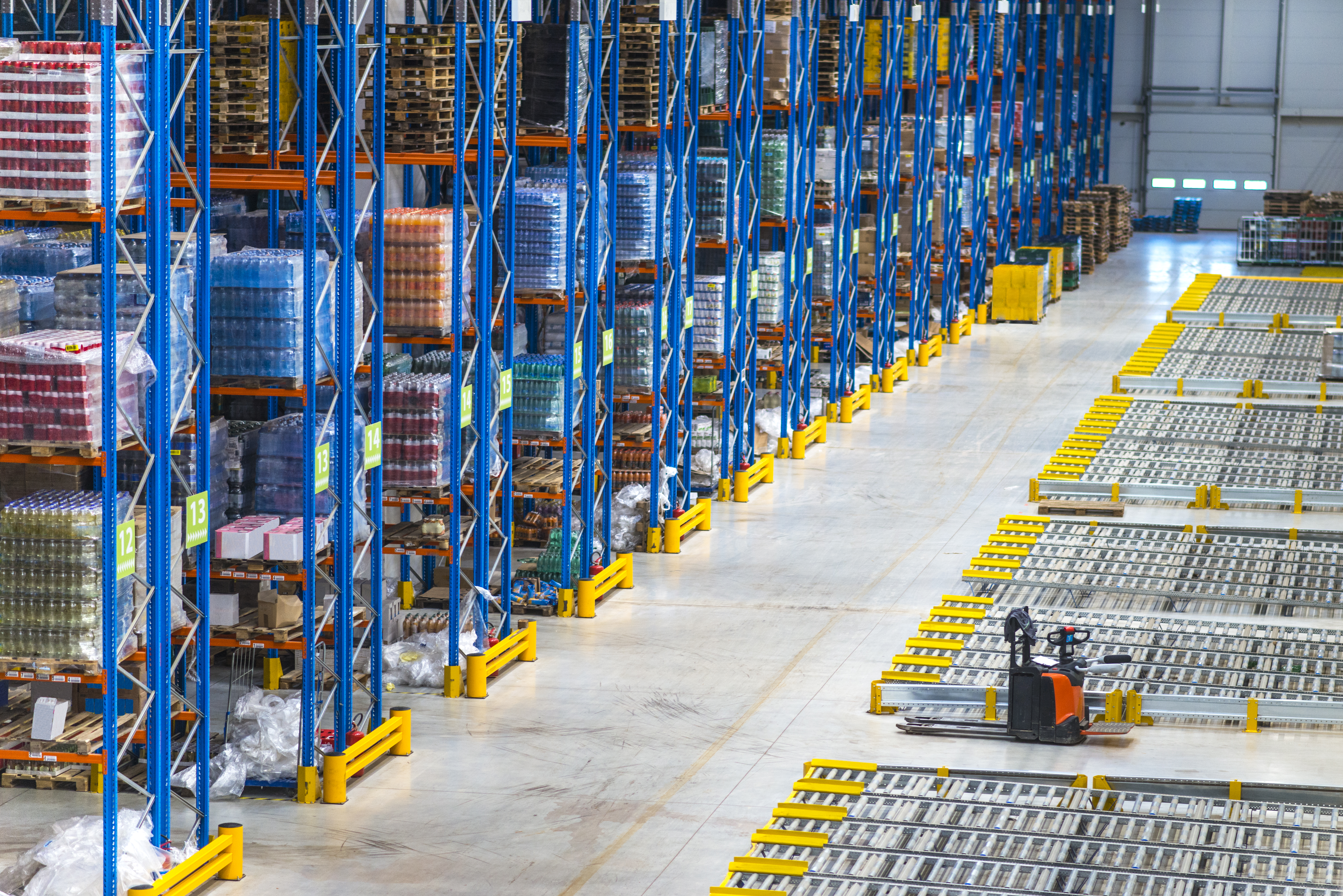 Interior of a large warehouse with tall blue pallet racking stacked with inventory and an orange pallet jack on the polished concrete floor.