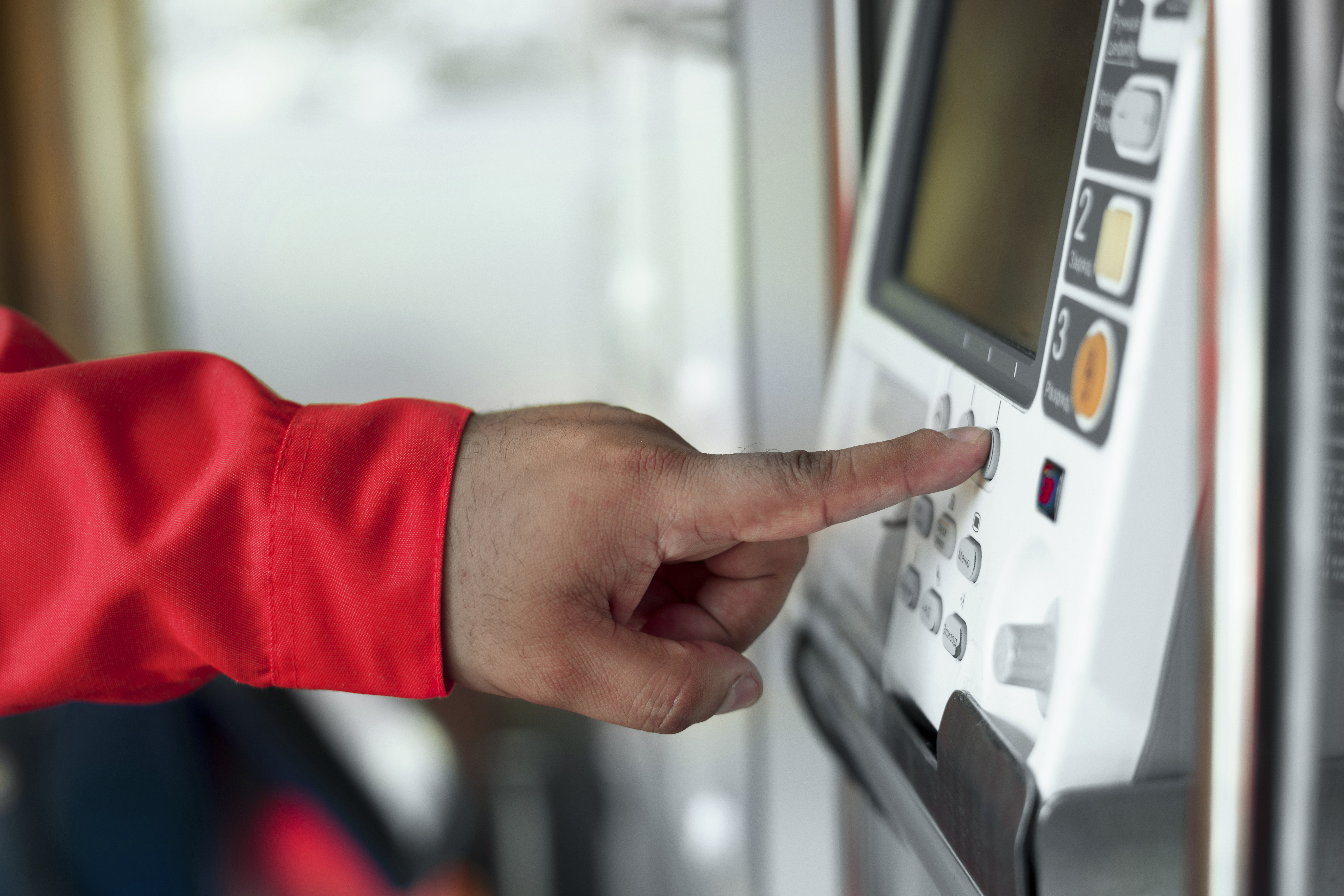 Technician in a red sleeve pressing buttons on a wall-mounted commercial fire alarm control panel.